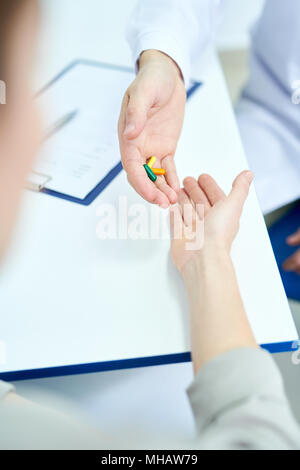 Primo piano di un irriconoscibile medico offrendo pillole per il giovane donna mentre è seduto alla scrivania in ufficio, spazio di copia Foto Stock