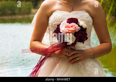 La sposa sta tenendo il fiore e dando una posa per una foto. I fiori viola sono fantastici. E la sposa si trova di fronte al bellissimo lago Foto Stock