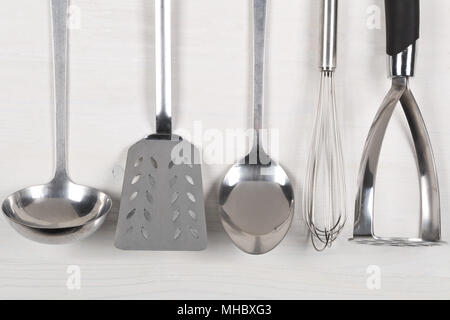 Riga di metallo utensili per la cucina con cucchiai e spatole da sopra il legno bianco sullo sfondo della scheda Foto Stock