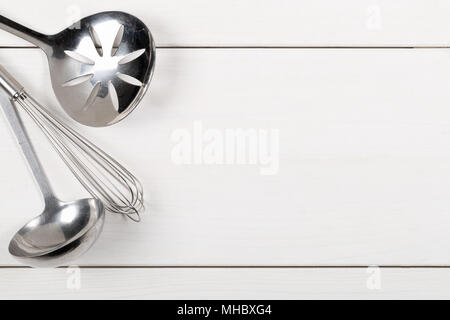 La cucina in metallo Utensili con cucchiaio, mescolando con una frusta e la spatola da sopra il legno bianco sullo sfondo della scheda Foto Stock