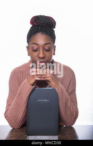 Un giovane americano africano donna orante oltre la Sacra Bibbia Foto Stock