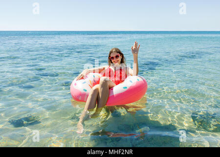 Happy brunette donna in rosa ciambella gonfiabile in estate giornata di sole. Foto Stock