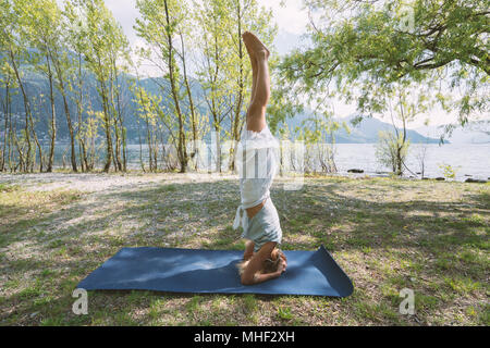 Giovane donna esercizio di yoga in riva al lago e montagne, girato in Canton Ticino, Svizzera, Europa. Persone relax benessere concept Foto Stock
