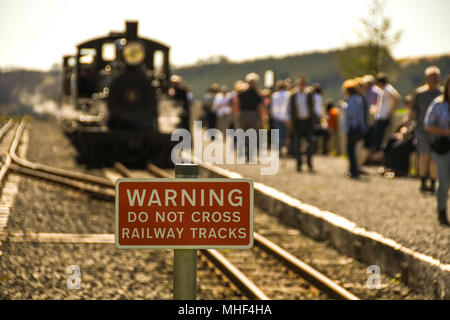 Segno sul Brecon ferrovia di montagna avviso di persone per tenere fuori pista, con un motore a vapore e i passeggeri in background Foto Stock