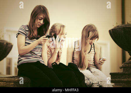 Un gruppo di ragazze adolescenti chiamando su telefoni cellulari per esterno Foto Stock