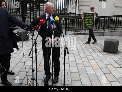 Michael Wardlow, commissario capo presso le uguaglianze Commissione, si prepara a parlare ai media come un uomo detiene una targhetta citando la Bibbia al di fuori della Royal Courts of Justice a Belfast dove la Corte suprema sta esaminando le questioni legate al Ashers Baking Company "gay torta" caso. Picture Data: martedì 1 maggio 2018. Vedere PA storia ULSTER torta. Foto di credito dovrebbe leggere: Brian Lawless/PA FILO Foto Stock