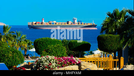 Un enorme nave cargo trasporta i contenitori con carico in Mar Rosso contro il cielo blu e verde brillante vegetazione vicino l'unico Ras Mohammed re della natura Foto Stock