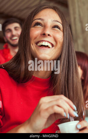 Giovani femmine sostenitore fan vestiti di rosso il colore rilassante bevendo una tazza di caffè in stand durante una partita Foto Stock