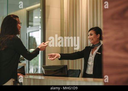 La donna alla reception a dare la sua carta di credito per addetta alla ricezione del pagamento. Ospiti di sesso femminile di pagare per la camera in hotel. Foto Stock