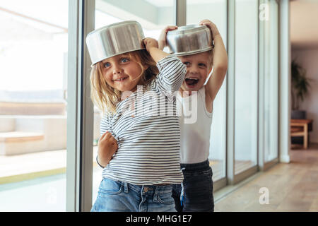 Carino bimbi piccoli indossando ciotola come casco e giocare in casa. I bambini giocano knight con un arnese da cucina. Foto Stock