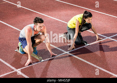 Maschio e femmina atleta in posizione di partenza al blocco di partenza Foto Stock