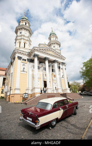 Uzhgorod, Ucraina - 18 Aprile 2015: veduta laterale della vecchia retrocar permanente sulla chiesa e sfondo con cielo nuvoloso. Auto è molto bella e accurata. La bellissima chiesa edificio architeckture. Guardando bene. Foto Stock