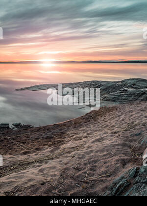 Sunset over Vänern, Mariestad, Svezia a Ekudden campeggio con la spiaggia e la costa rocciosa. Blu, arancione, rosa sky riflettendo nell'acqua. Foto Stock