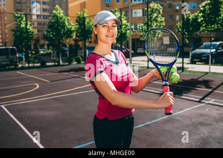 Primo piano vista frontale femmina giocatore di tennis prendendo una pausa durante una pratica su un caldo giorno d'estate in città. Donna sorridente con la videocamera e tenendo le sue dieci Foto Stock