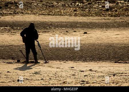 Un uomo profilarsi di rilevamento di metallo su una spiaggia di sabbia a sunrise presso la popolare località balneare di Llandudno, Wales, Regno Unito Foto Stock