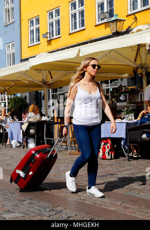 Copenhagen, Danimarca - 24 agosto 2017: una donna con lunghi capelli biondi che indossa un bianco top senza maniche, blue jeans e scarpe bianco richiama un rosso su ruote Foto Stock