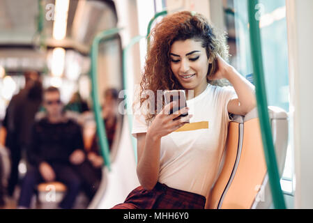 Arabo donna dentro la metropolitana guardando il suo smart phone. Ragazza araba in abiti casual. Foto Stock