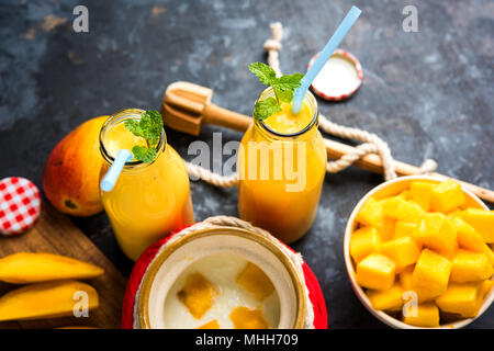 Mango Lassi o frappè in grande di vetro o bottiglie piccole con ricotta, tagliare la frutta in pezzi e frullatore. Moody sfondo, il fuoco selettivo Foto Stock