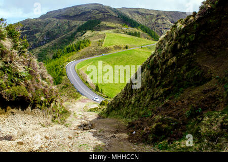 Andando su strada attraverso le montagne e colline verdi Foto Stock