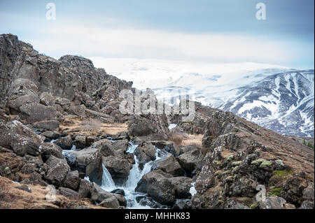 Paesaggio roccioso, bella cade con un innevate sullo sfondo di montagna vicino a cascata Drekkingarhylur, Thingvellir National Park, Islanda. Foto Stock