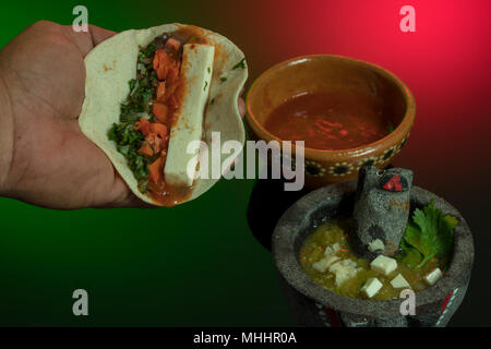Taco messicano sul tortilla di mais. I colori di bandiera si sono riflessi sul nero superficie acrilica. Hot salsa piccante al top è spento. Foto Stock