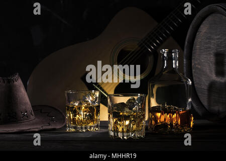 Due bicchieri di whiskey con ghiaccio e cappello da cowboy sulla tavola di legno Foto Stock