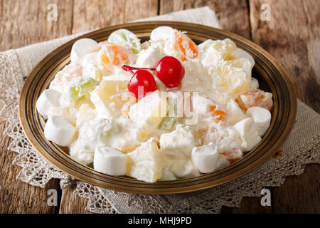 Insalata di frutta dal ananas, arance, uve e noce di cocco con marshmallow e yogurt alla vaniglia close-up su una piastra orizzontale. Foto Stock