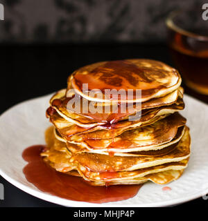 Pancake fatti in casa versato gocce di sciroppo in piastra bianca su sfondo scuro, primo piano Foto Stock