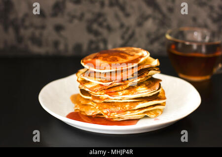 Pancake fatti in casa versato gocce di sciroppo in piastra bianca su sfondo scuro, primo piano Foto Stock