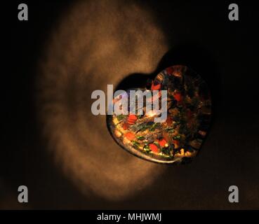 Fotografia di una resina Multi-Colored cuore in spotlight contro uno sfondo nero. Foto Stock