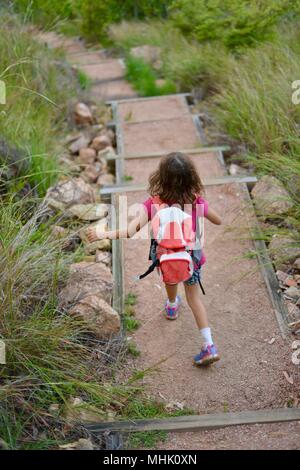 Scuola di giovani di età compresa tra la ragazza con uno zaino a piedi giù per le scale su un sentiero di ghiaia, Mount Stuart sentieri escursionistici, Townsville, Queensland, Australia Foto Stock