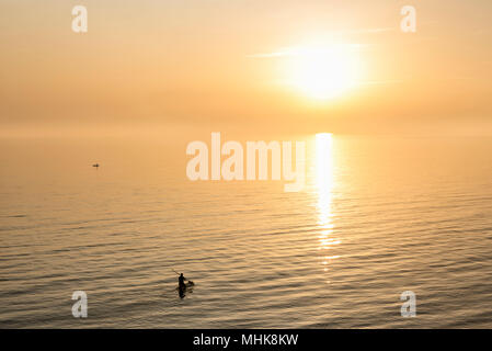 Silhouette di una persona pagaia a bordo del mare durante il tramonto Foto Stock
