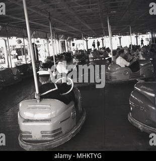 Anni sessanta, storico, persone a Battersea fun fair godendo i dodgems o del paraurti di automobili, Parco di Battersea, Londra, Inghilterra, Regno Unito. La fiera del divertimento è stato costruito nel parco come parte del 1951 Festival di Bretagna celebrazioni ed è stata una grande attrazione per i giovani e le famiglie in questa epoca. Il dodgem cavalcata fu di proprietà di e gestito da il botton Bros - il loro nome è sulle vetture - Albert e Jim Botton che crebbe in una fiera viaggio intorno a Londra e il sud dell'Inghilterra. Foto Stock