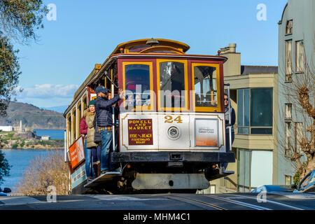 Street cable car - un cavo auto salendo fino alla cima della ripida collina russo su Hyde St, con l'Isola di Alcatraz in background. San Francisco, CA, Stati Uniti d'America. Foto Stock