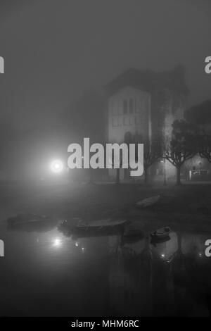 Alto edificio bianco riflesso nel lago su mattinata nebbiosa con illuminazione a Lampione Foto Stock