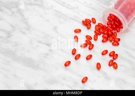 Bottiglia di Rosso di pillole lucido su sfondo marmo. Capsule la fuoriuscita del contenitore. Foto Stock