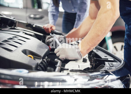 Un meccanico di uomo e donna il cliente guarda il cofano per auto e discutere le riparazioni Foto Stock