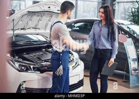 Il marito meccanico di automobili e la donna cliente a effettuare un accordo sulla riparazione dell'auto Foto Stock