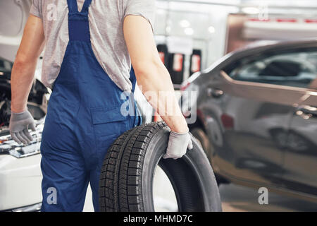 Mechanic tenendo un pneumatici presso il garage di riparazione. sostituzione delle gomme invernali ed estive Foto Stock