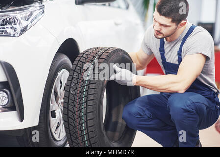 Mechanic tenendo un pneumatici presso il garage di riparazione. sostituzione delle gomme invernali ed estive Foto Stock