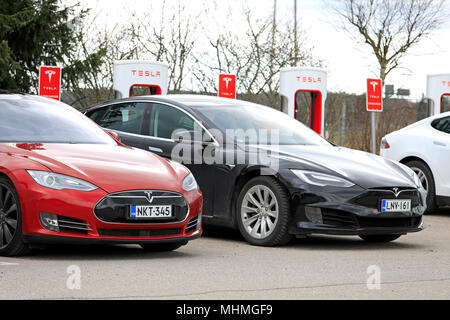 Due Tesla Model S auto elettriche, rosso del design precedente, nero di design aggiornato, sono in carica batteria a Supercharger station su un giorno di primavera Foto Stock