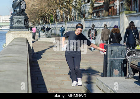 Plogging UK. Donna jogging lungo Southbank sul fiume a Londra, prelievo e gettare via i rifiuti in una cucciolata bin. Foto Stock