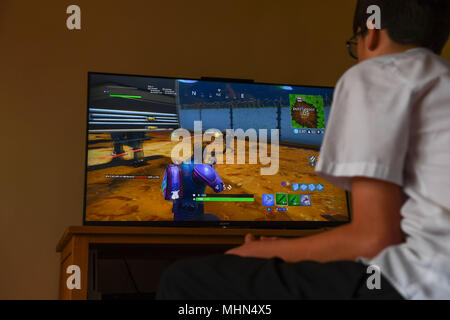 Un ragazzo adolescente gioca il colpo computer game Fortnite su un TV di grandi dimensioni su una Playstation 4 Console. Foto Stock