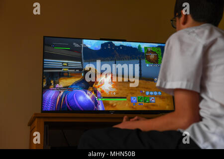 Un ragazzo adolescente gioca il colpo computer game Fortnite su un TV di grandi dimensioni su una Playstation 4 Console. Foto Stock