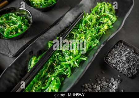 Le alghe wakame insalata servita con baguette su sfondo nero Foto Stock