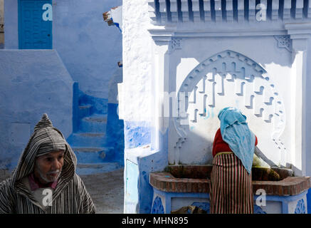 Chefchaouen, Marocco; l uomo e la donna in abito tradizionale a fontana pubblica nella città vecchia. Foto Stock