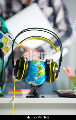 Globo terrestre è sul tavolo per cuffie. Interno dell'appartamento. Un ragazzo con un laptop in mano sullo sfondo Foto Stock