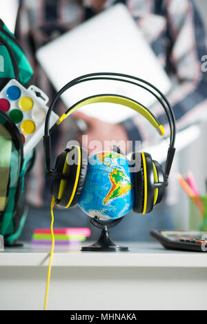 Globo terrestre è sul tavolo per cuffie. Interno dell'appartamento. Un ragazzo con un laptop in mano sullo sfondo Foto Stock