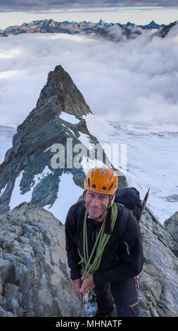 Scalatore moutain voce da un picco ad un altro in alta montagna delle Alpi svizzere con un mare di nuvole dietro di lui Foto Stock