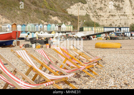 Una fila di vuoto tradizionale telaio in legno sedie a sdraio con il rosso e bianco striato materiale su una spiaggia di ciottoli con ombrelloni e chalk cliffs nel retro Foto Stock